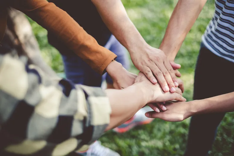 Mehrere Menschen legen ihre Hände übereinander als Zeichen von Teamarbeit und Zusammenhalt